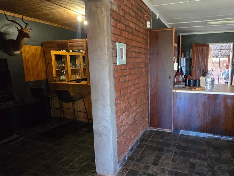 Open plan living area featuring a built-in bar, exposed brick wall, and kitchen space with dark cabinetry and tiled flooring.