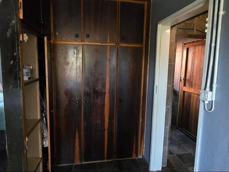 Bedroom featuring dark wood built-in cupboards and tiled flooring, with an adjacent doorway leading to an en-suite bathroom.