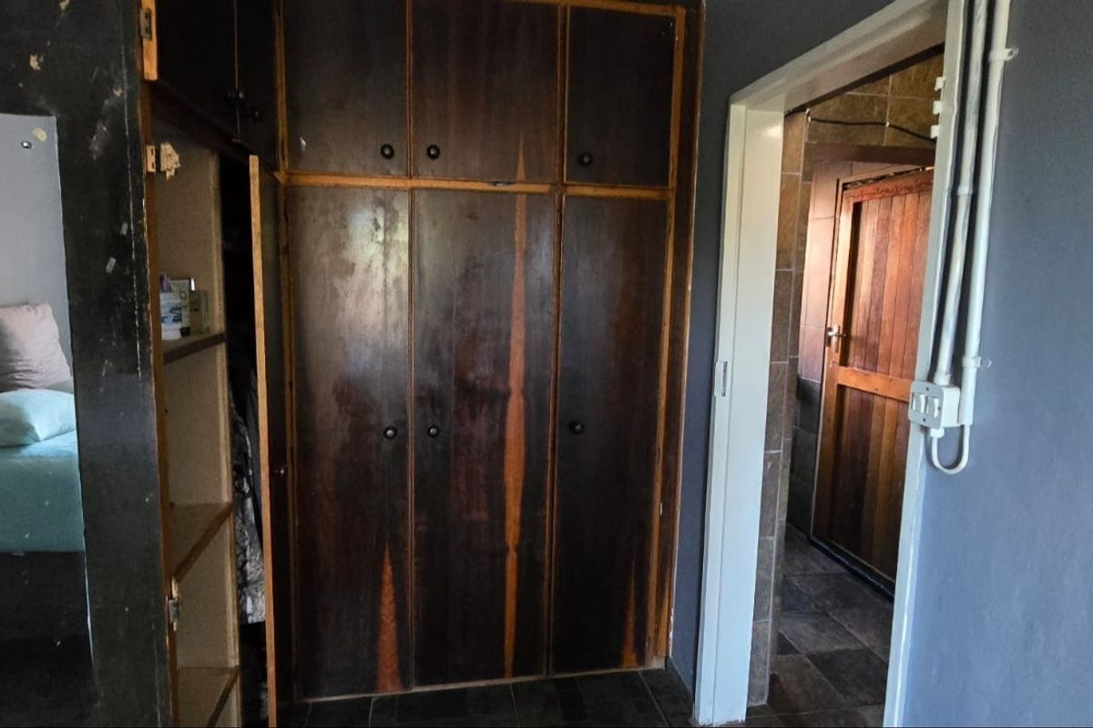 Bedroom featuring dark wood built-in cupboards and tiled flooring, with an adjacent doorway leading to an en-suite bathroom.
