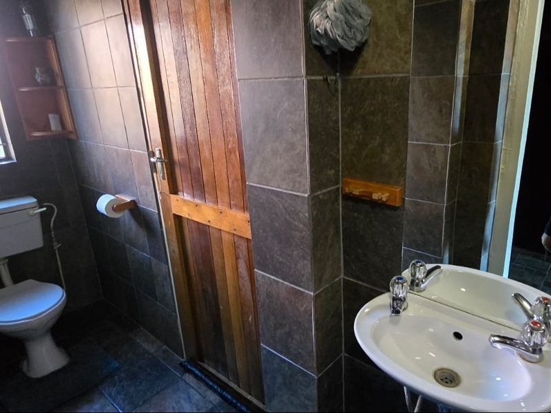 A functional bathroom featuring dark tiled walls and flooring, a pedestal basin, and a timber door.