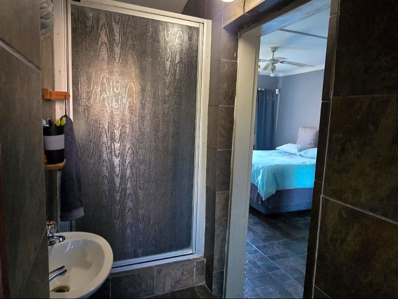 A functional bathroom featuring a shower enclosure and pedestal basin, with dark tiled finishes, providing direct access to the adjacent bedroom.