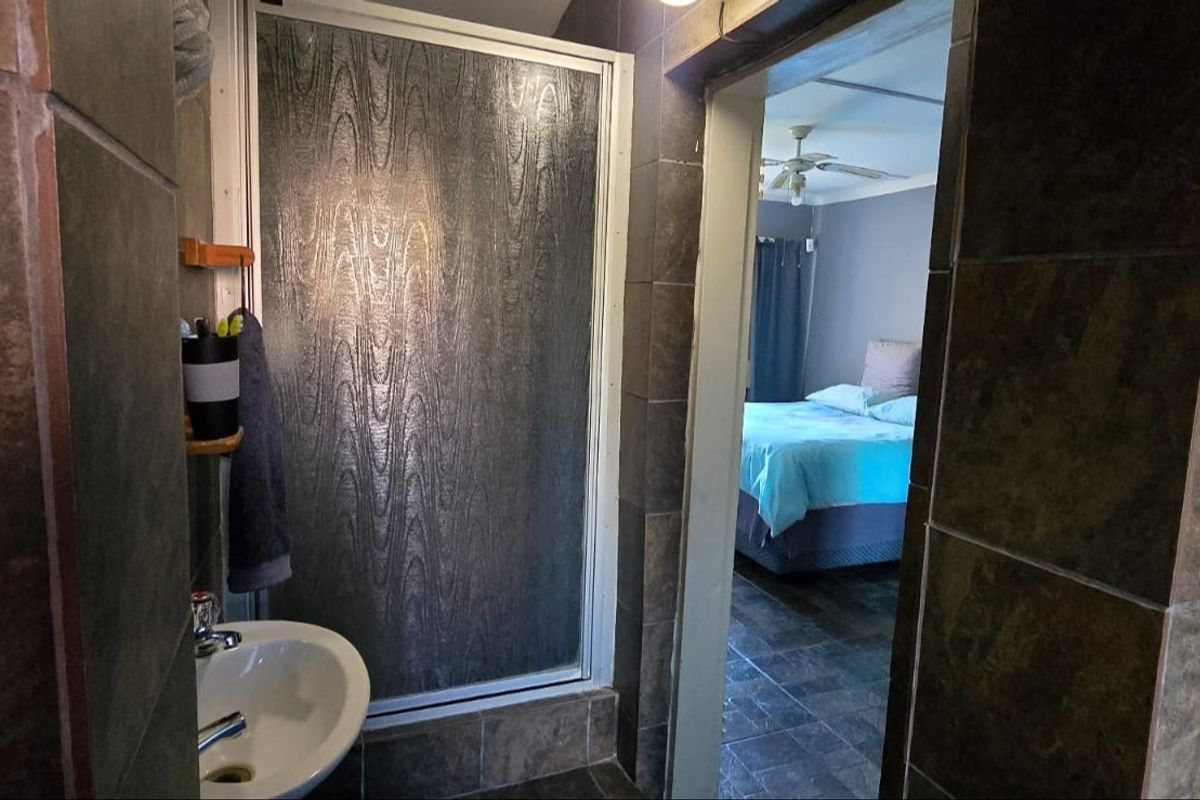 A functional bathroom featuring a shower enclosure and pedestal basin, with dark tiled finishes, providing direct access to the adjacent bedroom.