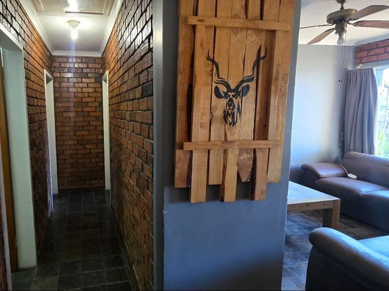 Open plan living area featuring exposed brick walls, tiled flooring, a ceiling fan, and a wall-mounted air conditioning unit.