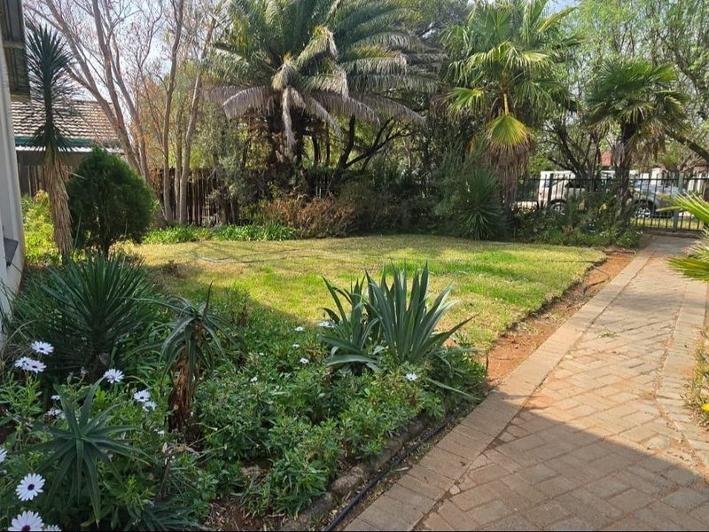 A well-maintained garden featuring a paved walkway, established trees, and lush greenery, providing a pleasant outdoor space.