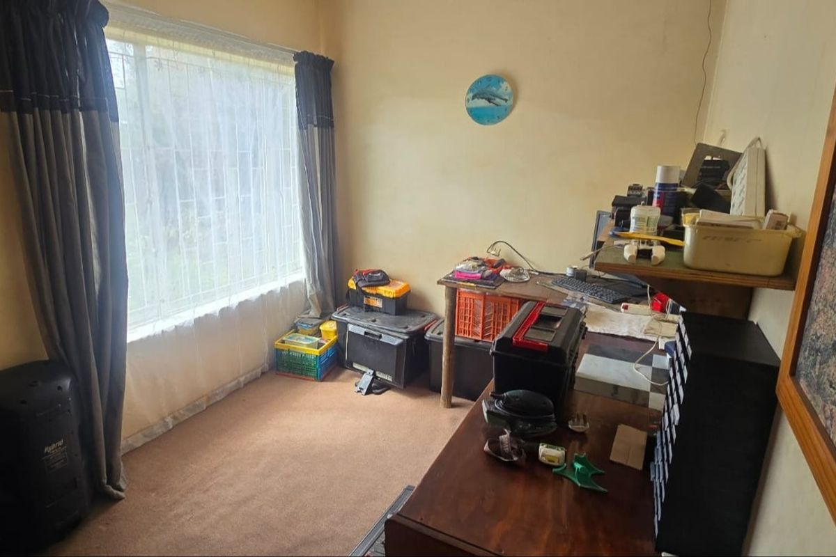 A bedroom featuring a large window and carpet flooring, currently utilized as a workspace with potential for renovation and modernization.