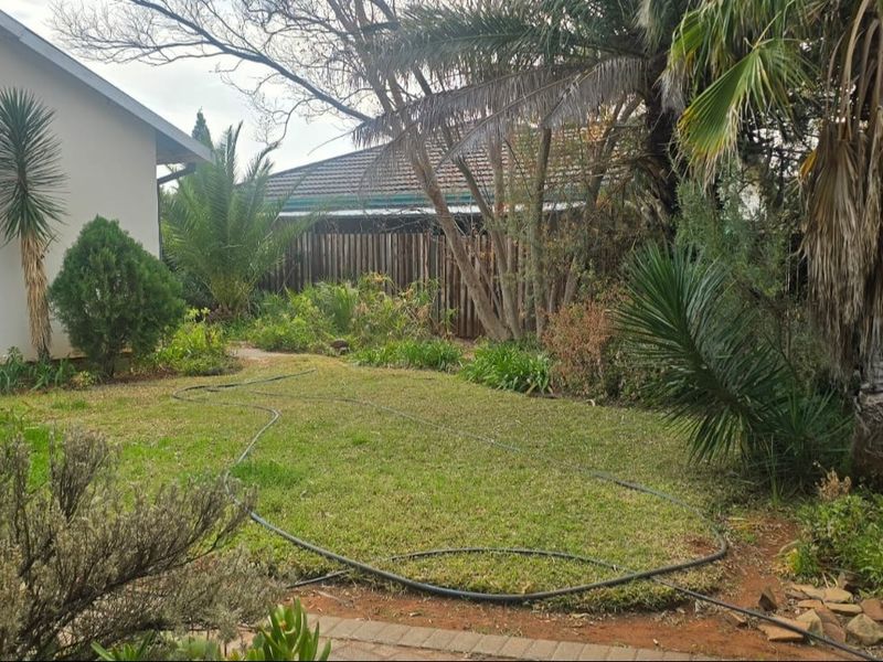 A private rear garden featuring a lawn area, mature trees, and a timber boundary fence.
