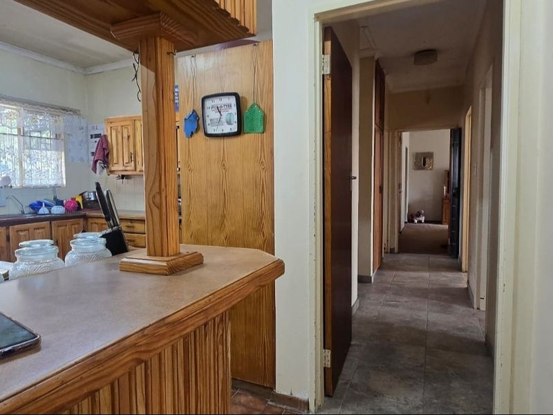 A dated kitchen featuring wooden cabinetry and a breakfast bar, leading into a hallway with tiled flooring.