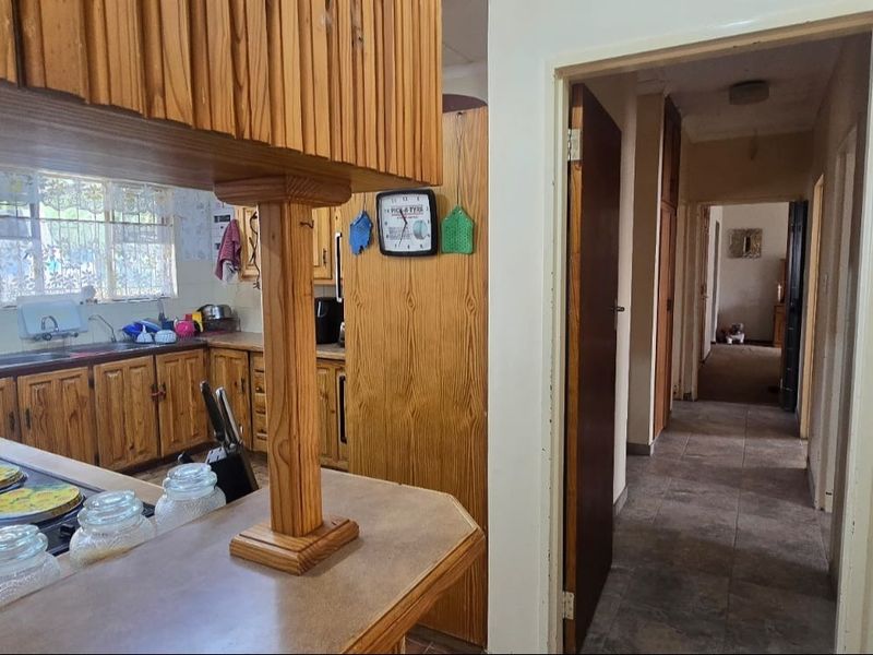 A dated kitchen featuring wooden cabinetry and a breakfast bar, leading into a tiled hallway with access to other rooms.