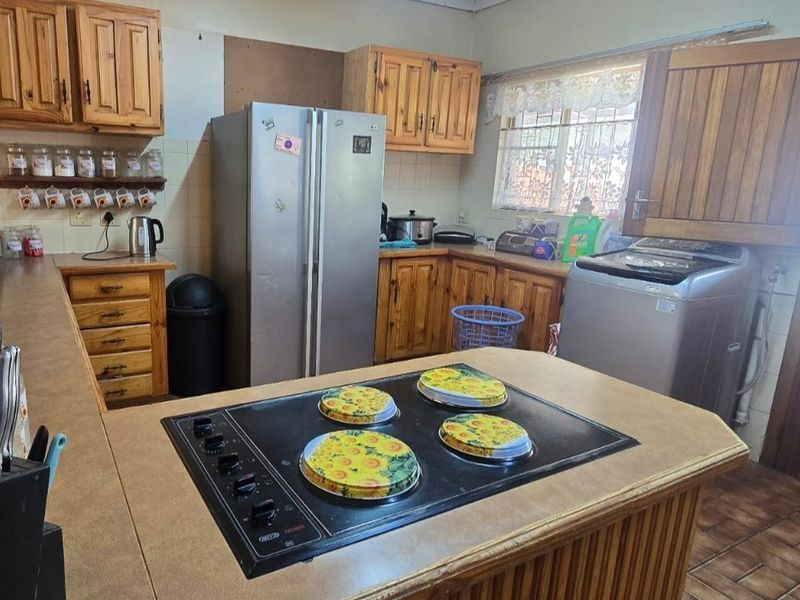 A dated kitchen featuring wooden cabinetry, laminate countertops, and a built-in electric hob, offering potential for a modern renovation.