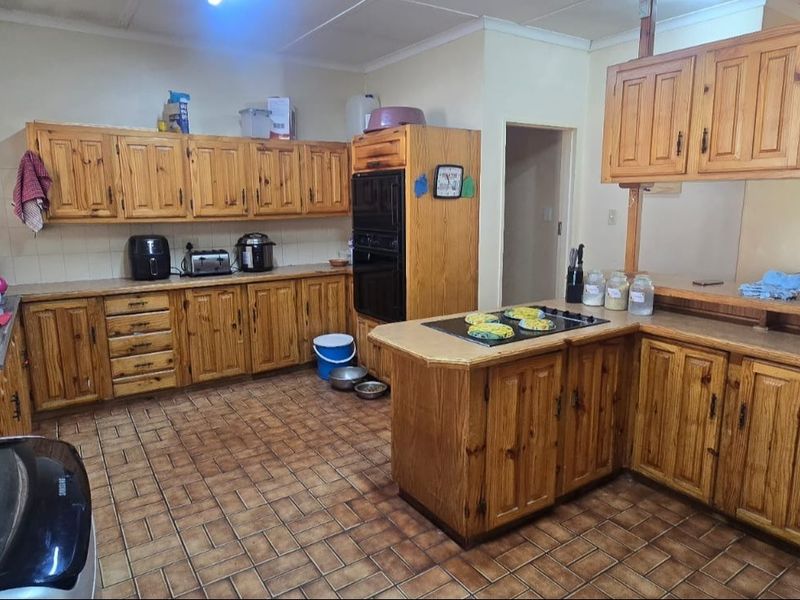 A spacious kitchen featuring extensive wooden cabinetry, a built-in oven, electric hob, and tiled flooring, offering a functional layout with ample storage space.