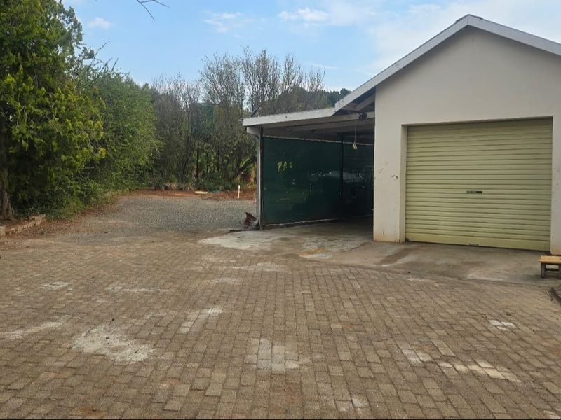 Exterior view of a garage with a roller shutter door, adjacent carport, and paved driveway area.