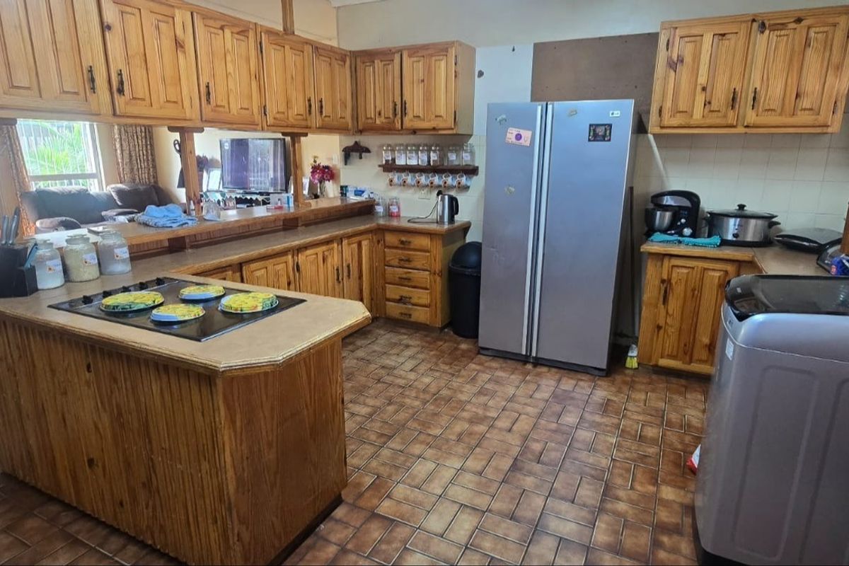 A spacious kitchen featuring extensive wooden cabinetry, a central breakfast counter with a built-in hob, and tiled flooring throughout.