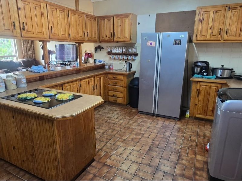A spacious kitchen featuring extensive wooden cabinetry, a central breakfast counter with a built-in hob, and tiled flooring throughout.