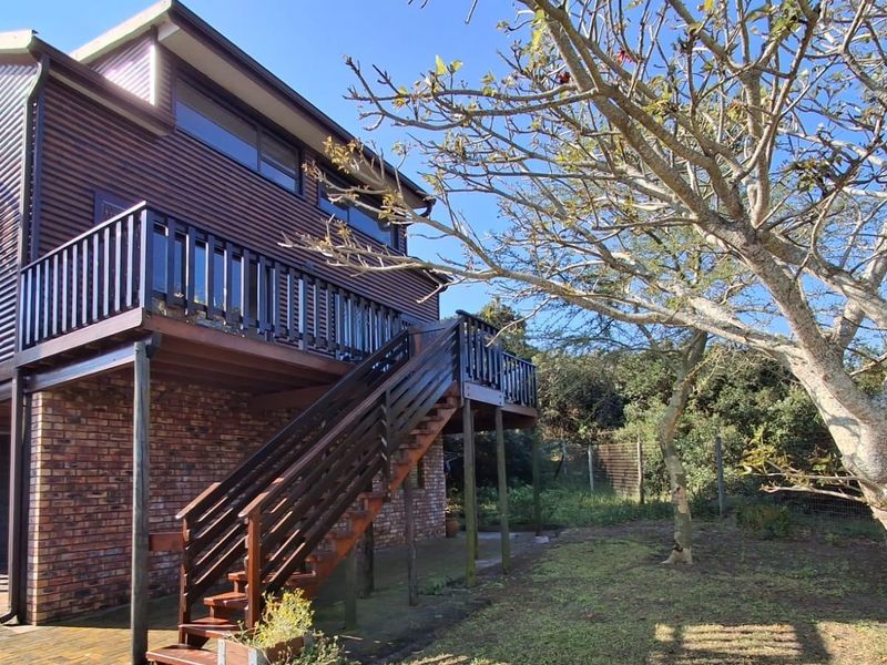 Rear view of a multi-level house featuring a timber deck, external staircase, and brick foundation set within a garden area.