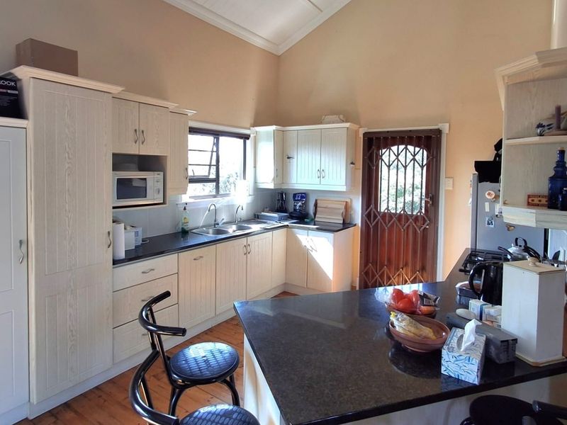 A functional kitchen featuring light-toned cabinetry, dark granite countertops, a double basin sink, and vaulted ceilings with timber flooring.