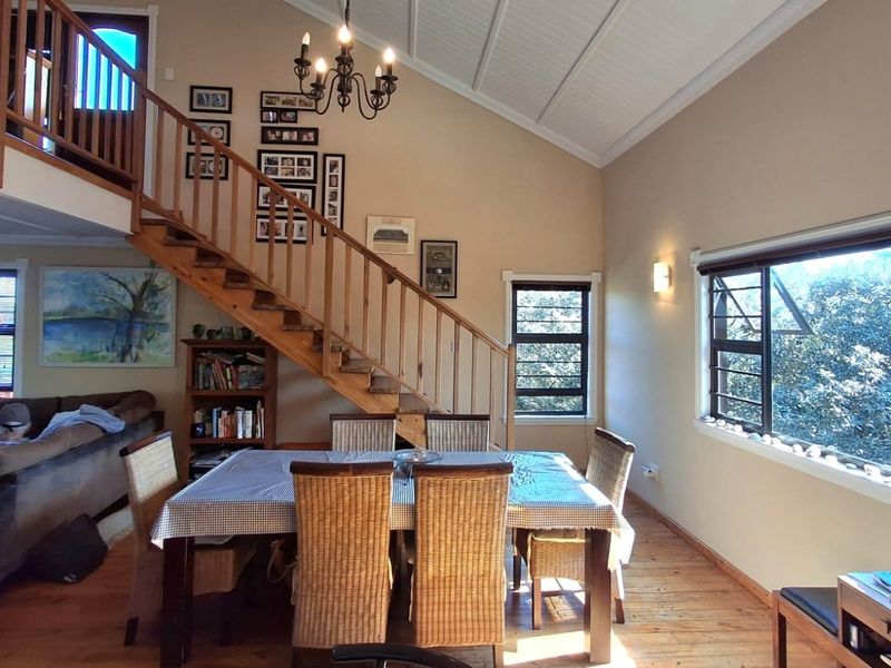 Open plan dining area featuring timber flooring, a vaulted ceiling, and a prominent timber staircase leading to an upper level.