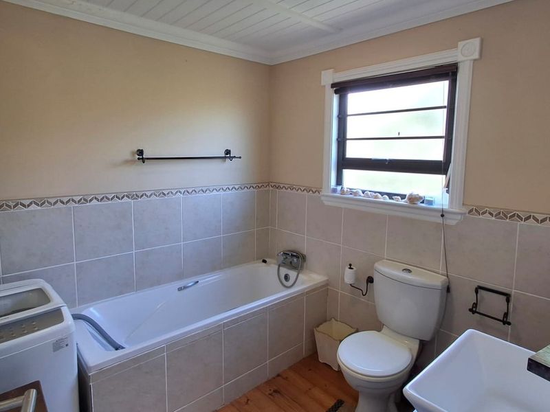 A functional bathroom featuring a bathtub, toilet, basin, tiled wall accents, and timber flooring, providing a practical layout for daily use.
