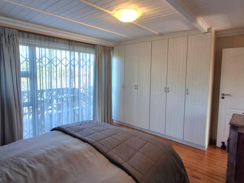 A well-maintained bedroom featuring timber flooring, extensive built-in cupboards, and a sliding glass door providing access to an outdoor area.
