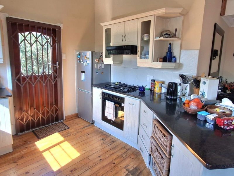 A functional kitchen featuring timber flooring, stone countertops, built-in cabinetry, and integrated gas hob and oven, with direct access to an exterior security door.