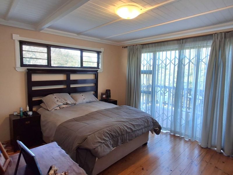 A bedroom featuring timber flooring, exposed beam ceiling, and a sliding glass door with a security gate leading to an outdoor area.