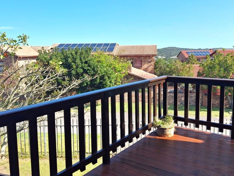 An elevated timber balcony featuring a wooden balustrade, overlooking a residential garden area with surrounding properties.