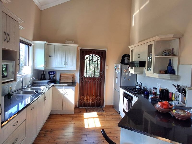 A functional kitchen featuring timber flooring, granite countertops, built-in cabinetry, and a gas hob with an extractor fan.