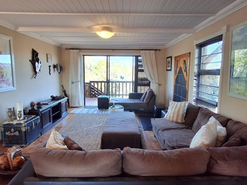 A comfortable living room featuring timber flooring, a white tongue and groove ceiling, and sliding glass doors leading to an outdoor deck.