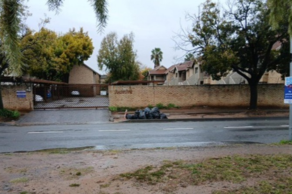Street view of the townhouse complex entrance featuring a brick boundary wall, gated driveway access, and covered parking structures.