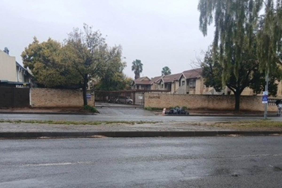 Street view of the townhouse complex entrance featuring a perimeter brick wall and security gate access from the main road.