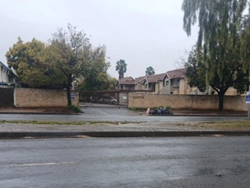 Street view of the townhouse complex entrance featuring a perimeter brick wall and security gate access from the main road.