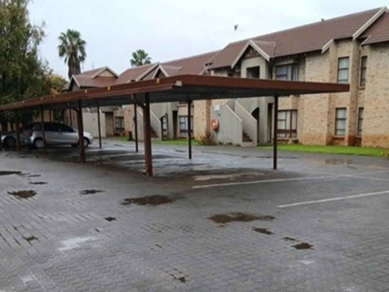 Exterior view of the townhouse complex featuring a covered carport area and paved driveway with brick facade building architecture.