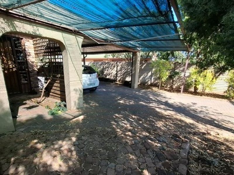 Front exterior view featuring a paved driveway and a covered carport area with shade cloth structure.