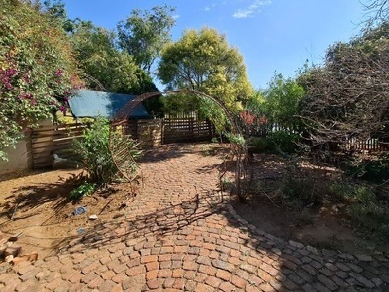 A garden area featuring cobblestone paving, a decorative metal archway, and established perimeter fencing, offering potential for landscaping and outdoor improvement.