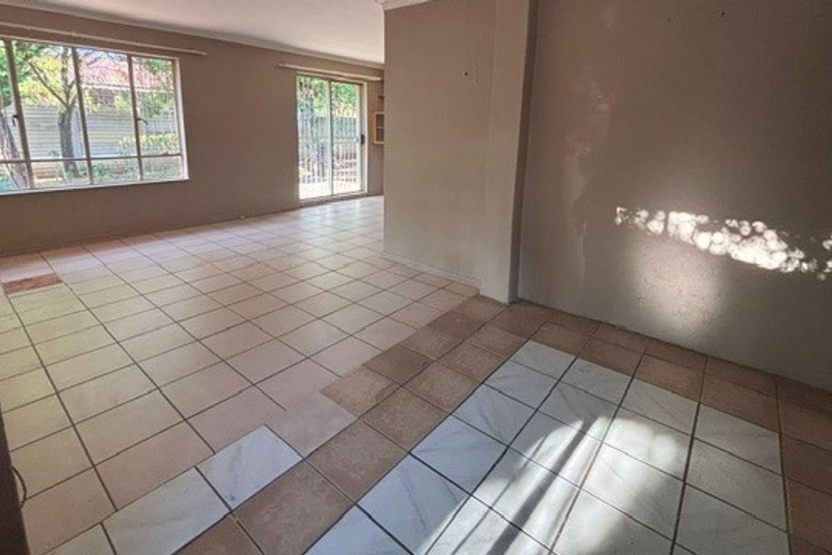 An empty, open-plan living area featuring tiled flooring, large windows, and a sliding glass door leading to the exterior.