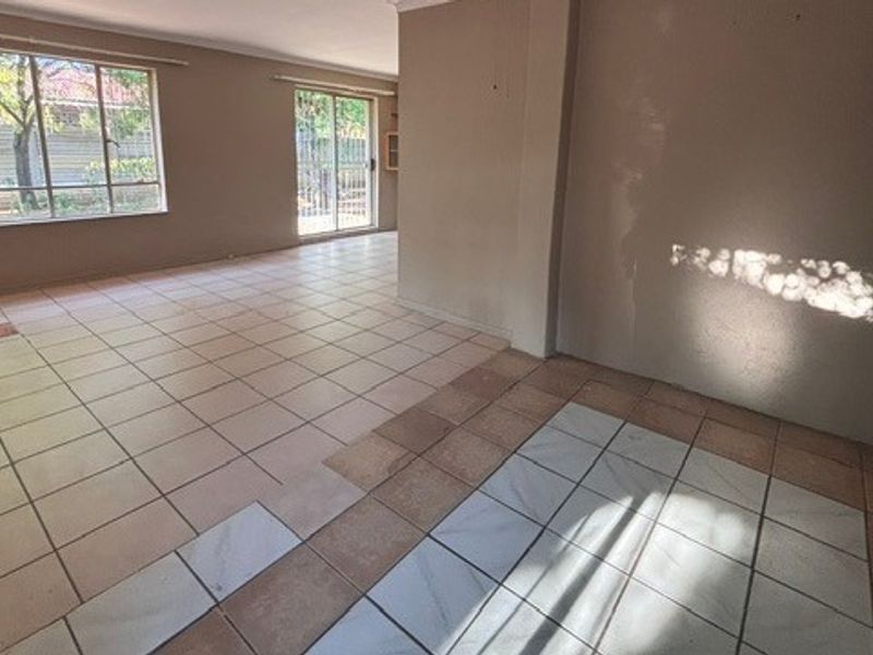 An empty, open-plan living area featuring tiled flooring, large windows, and a sliding glass door leading to the exterior.
