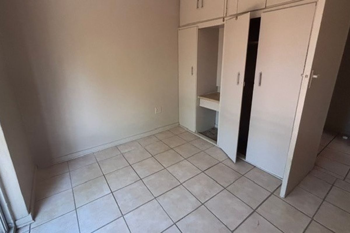An empty bedroom featuring tiled flooring, built-in cupboards, and a sliding door providing access to the exterior.