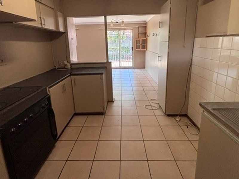 A functional kitchen featuring tiled flooring, built-in cabinetry, and a tiled backsplash, leading through to an open-plan living area with sliding door access.