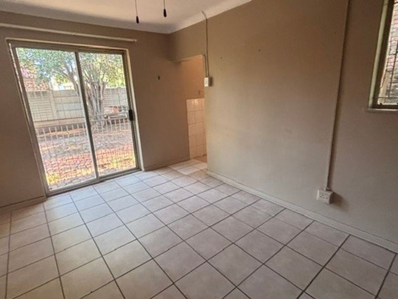 An empty living room featuring tiled flooring, a sliding glass door leading to the exterior, and a window with security bars.