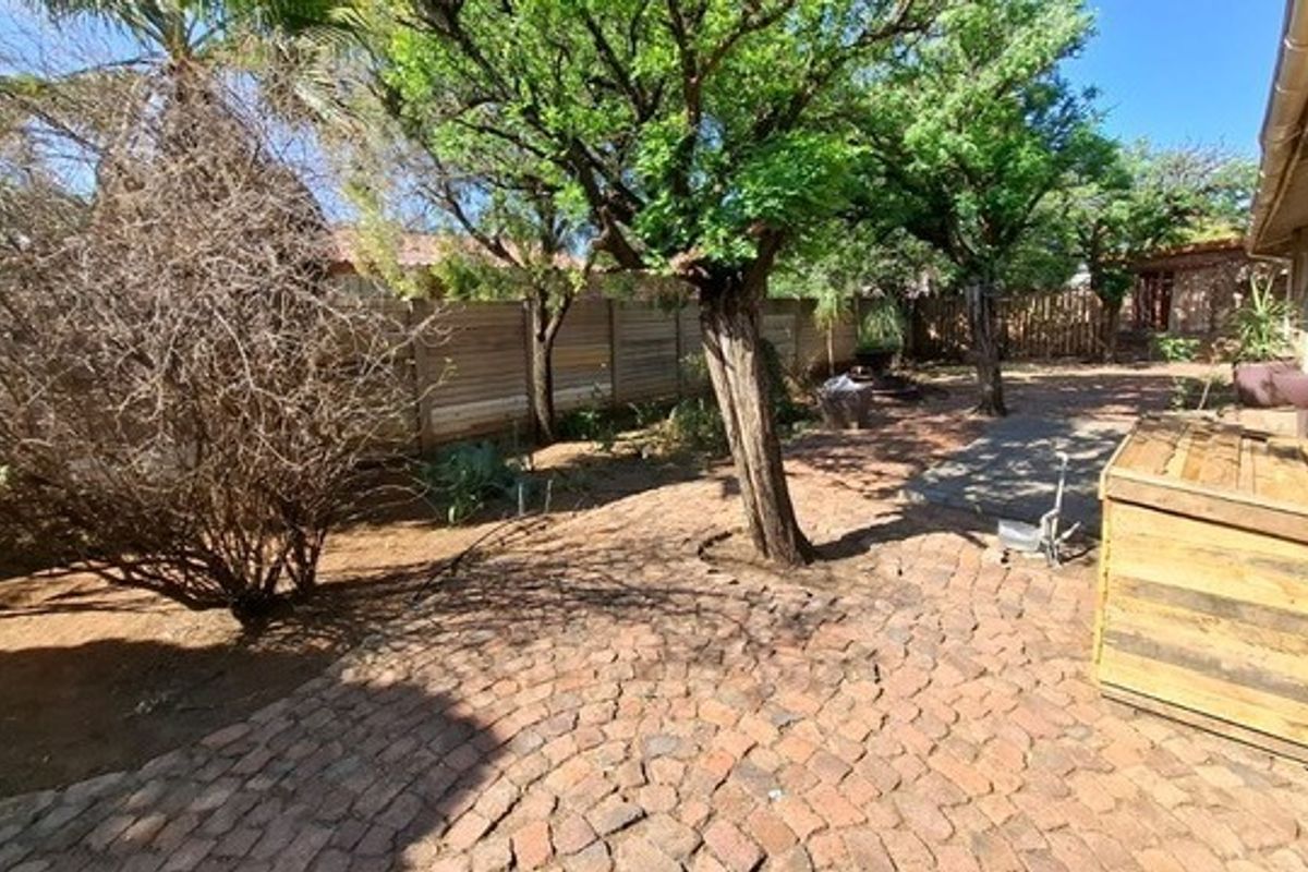 A rear garden area featuring brick paving, mature trees, and timber boundary fencing.