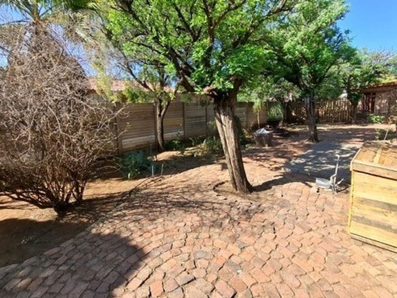 A rear garden area featuring brick paving, mature trees, and timber boundary fencing.