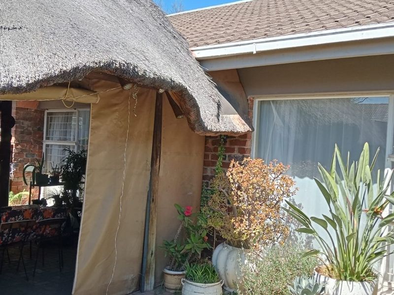 A covered patio area featuring a traditional thatched roof, brick masonry, and access to the main dwelling through a sliding glass door.