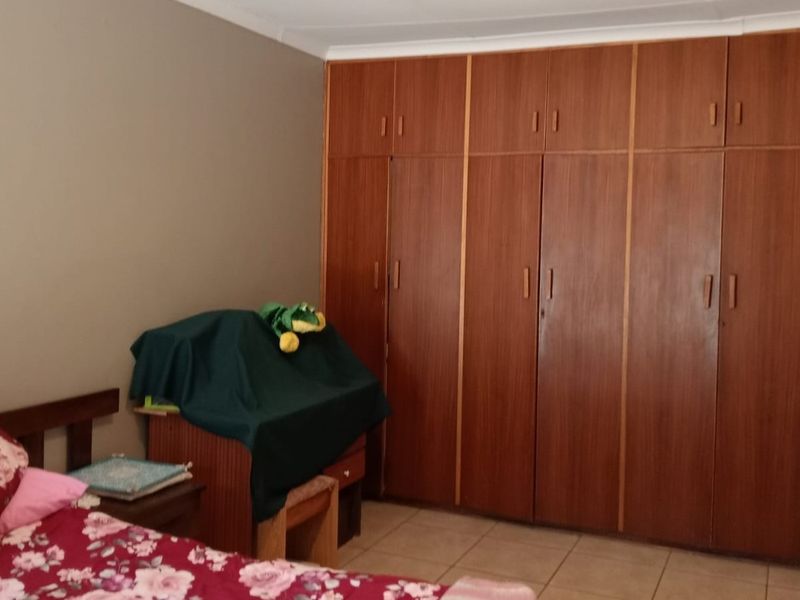 A bedroom featuring tiled flooring and extensive floor-to-ceiling built-in wooden cupboards providing ample storage space.