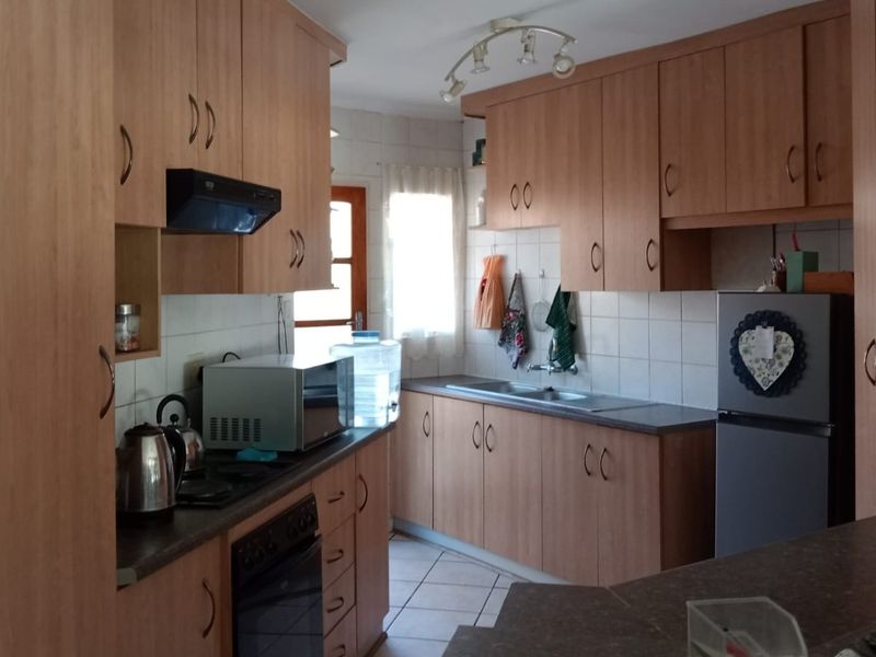 A functional kitchen featuring wood-look laminate cabinetry, tiled backsplash, built-in oven with extractor fan, and tiled flooring.
