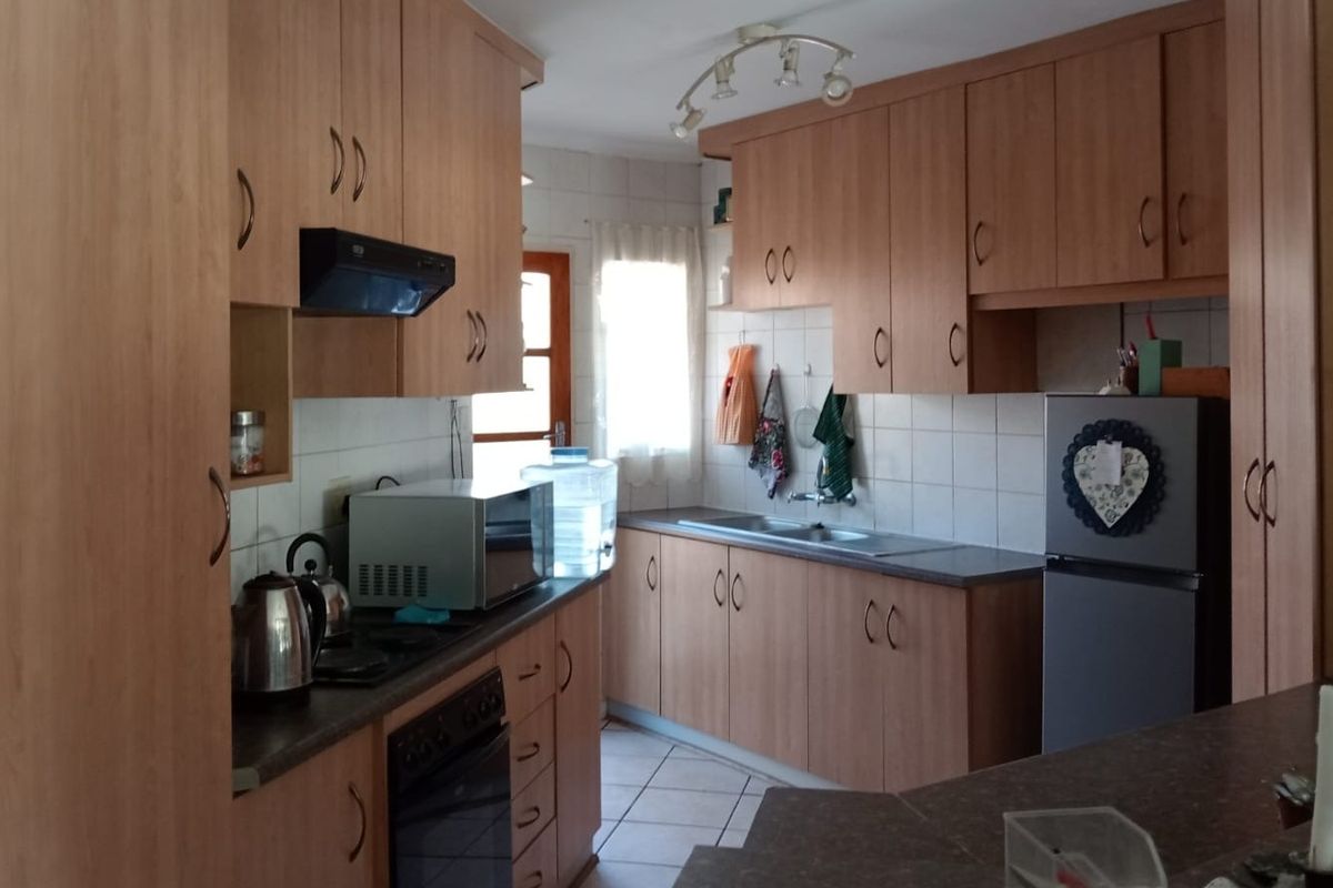 A functional kitchen featuring wood-look laminate cabinetry, tiled backsplash, built-in oven with extractor fan, and tiled flooring.