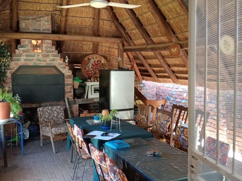 Covered outdoor patio area featuring a traditional thatched roof, exposed timber rafters, and a built-in brick fireplace and braai facility.