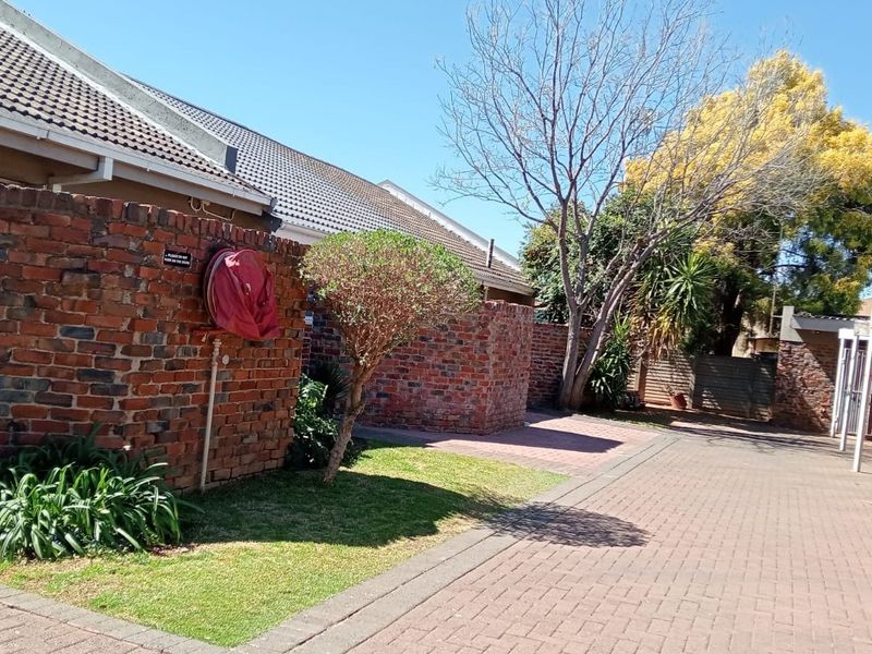 Exterior view of a townhouse complex featuring a paved driveway, brick boundary walls, and a covered carport area.