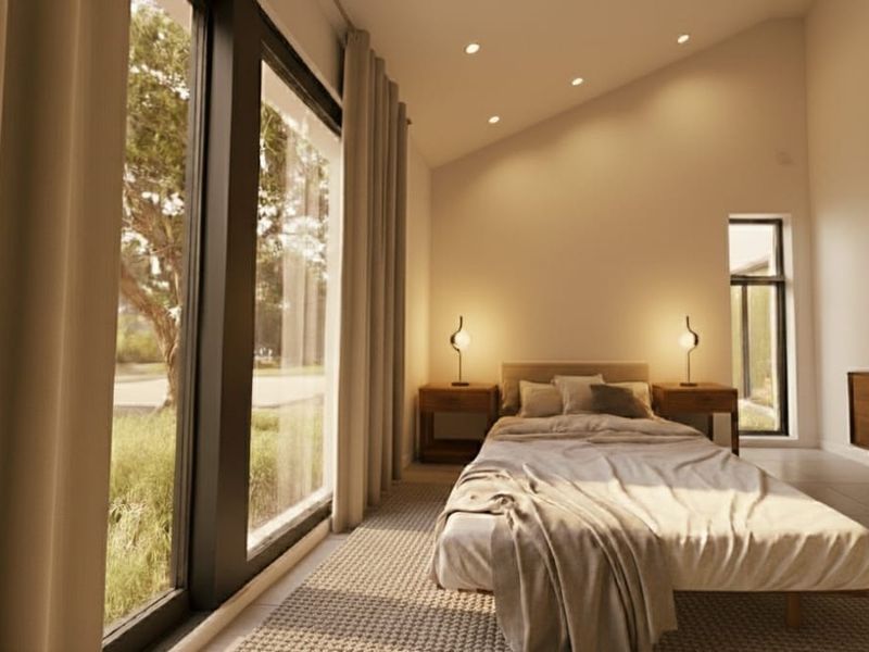 A bright, modern bedroom featuring a raked ceiling, recessed lighting, and large sliding glass doors that provide ample natural light and garden views.