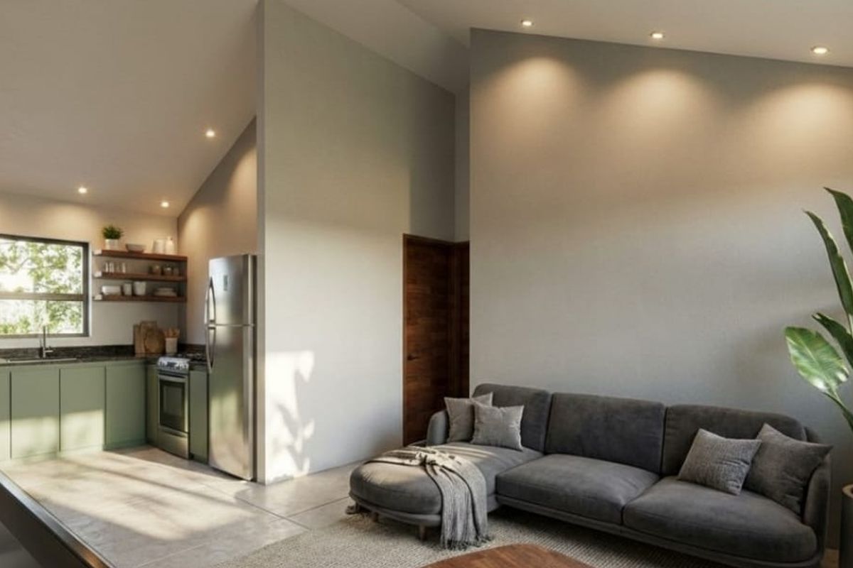 Modern open-plan living area featuring a compact kitchen with green cabinetry, sloped ceilings, recessed lighting, and seamless tiled flooring throughout.