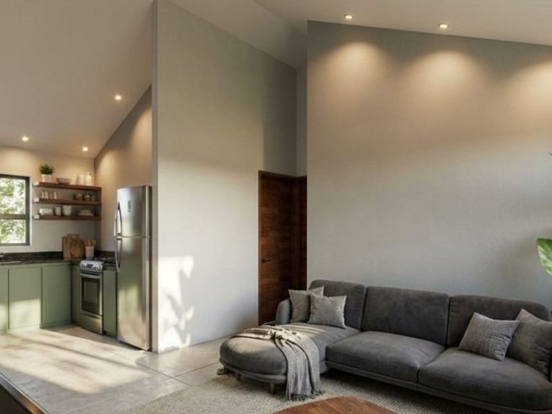 Modern open-plan living area featuring a compact kitchen with green cabinetry, sloped ceilings, recessed lighting, and seamless tiled flooring throughout.