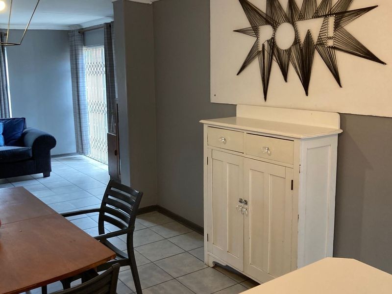 Open plan living and dining area featuring neutral grey walls, ceramic floor tiles, and access to an outdoor area via a sliding security gate.